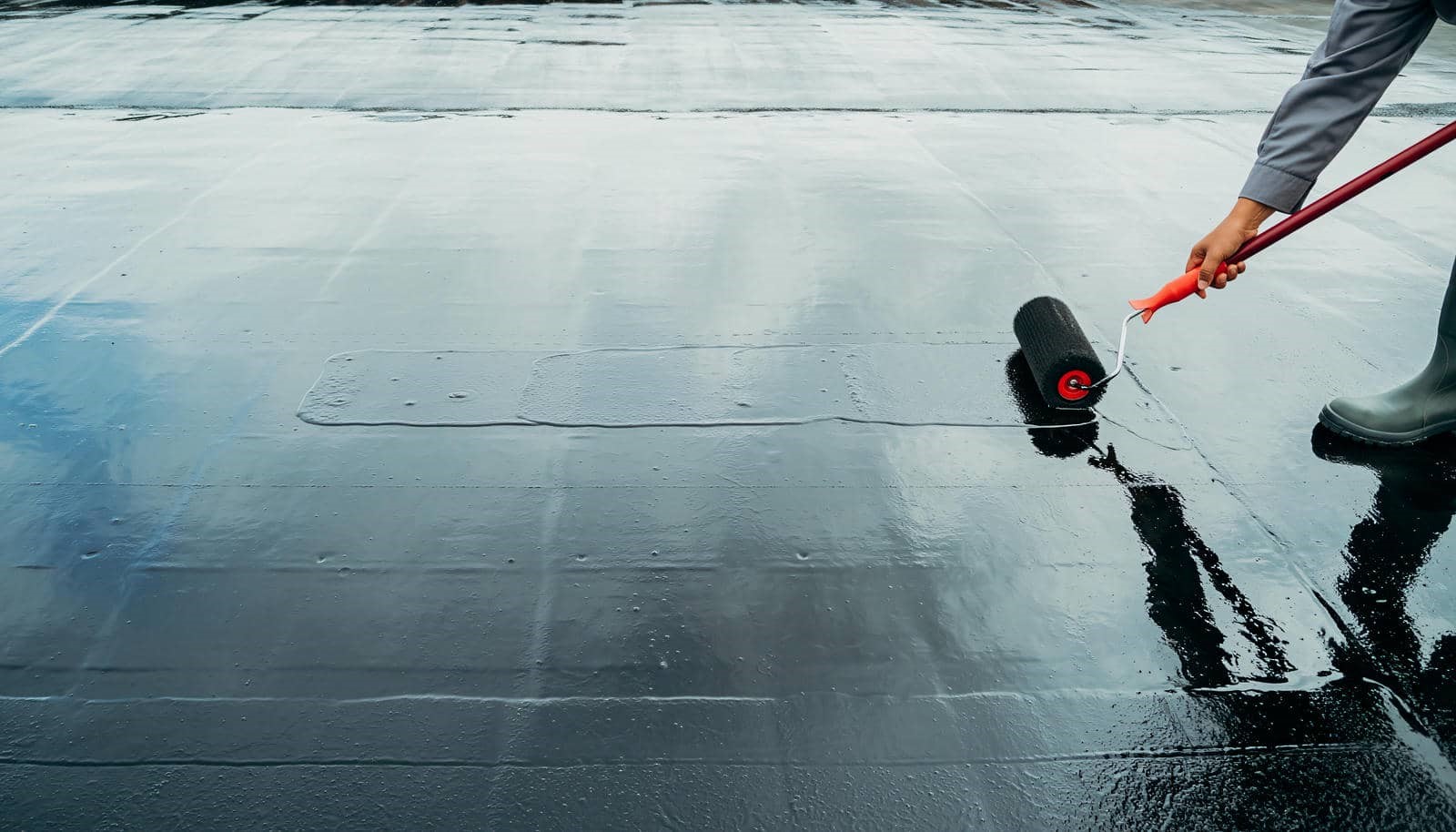 Applying coating on flat roof|Person standing on a wet