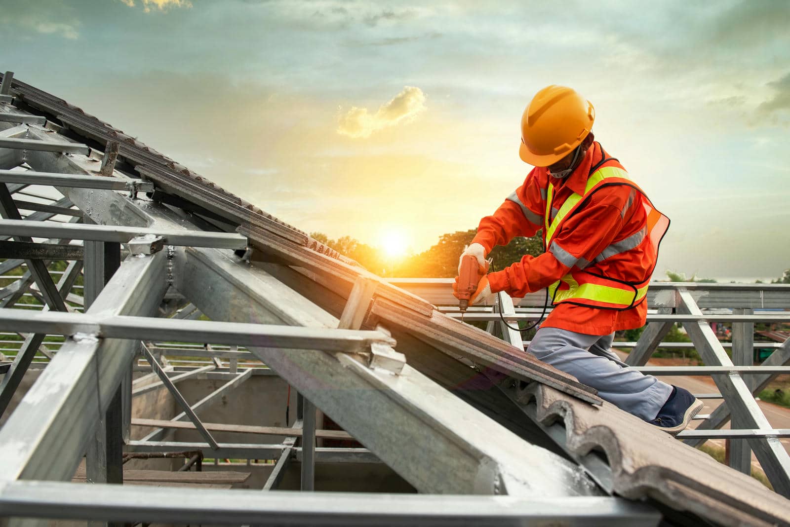 Construction worker in safety gear installing roof tiles at sunset.