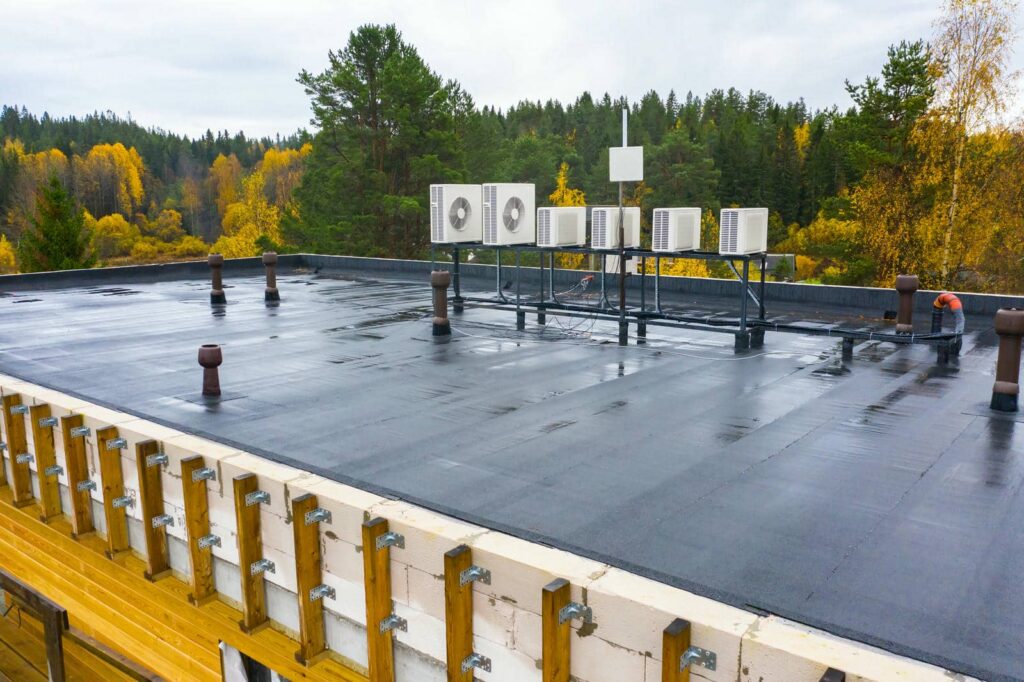 Flat black rooftop with multiple air conditioning units and forest trees in the background.