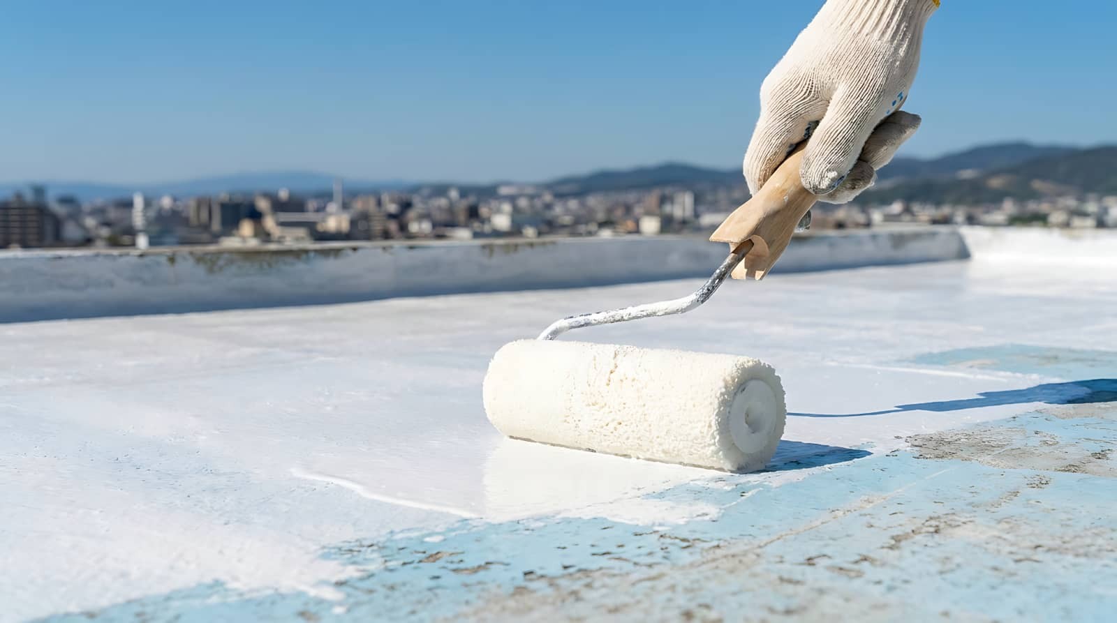 Gloved hand painting a rooftop with a paint roller.