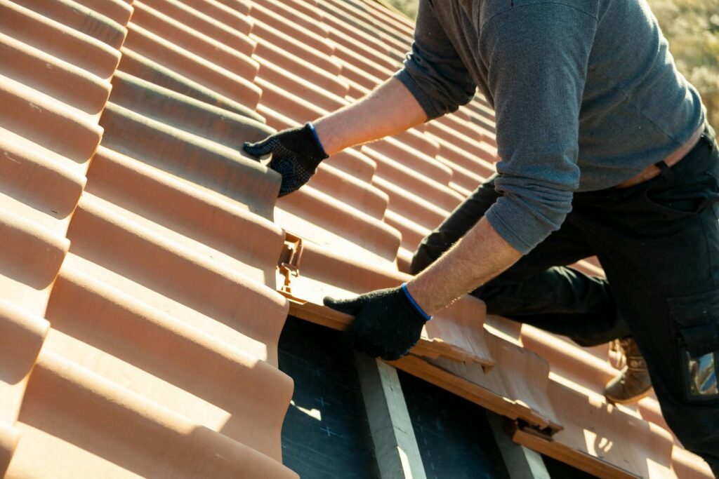 Person wearing gloves installing terracotta roof tiles on a sloped roof.