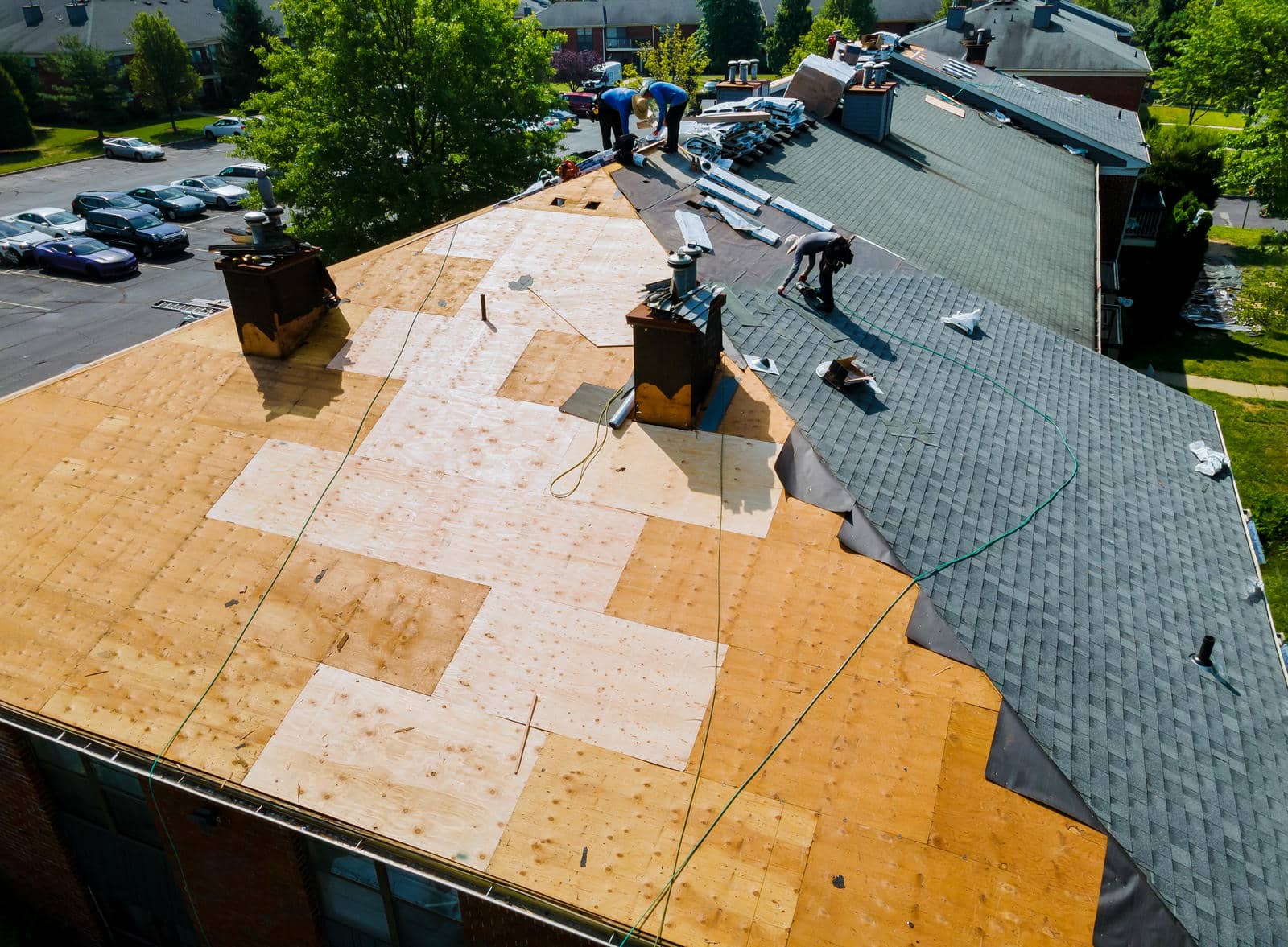 Workers installing new shingles on a large roof with exposed wooden panels and roofing materials.