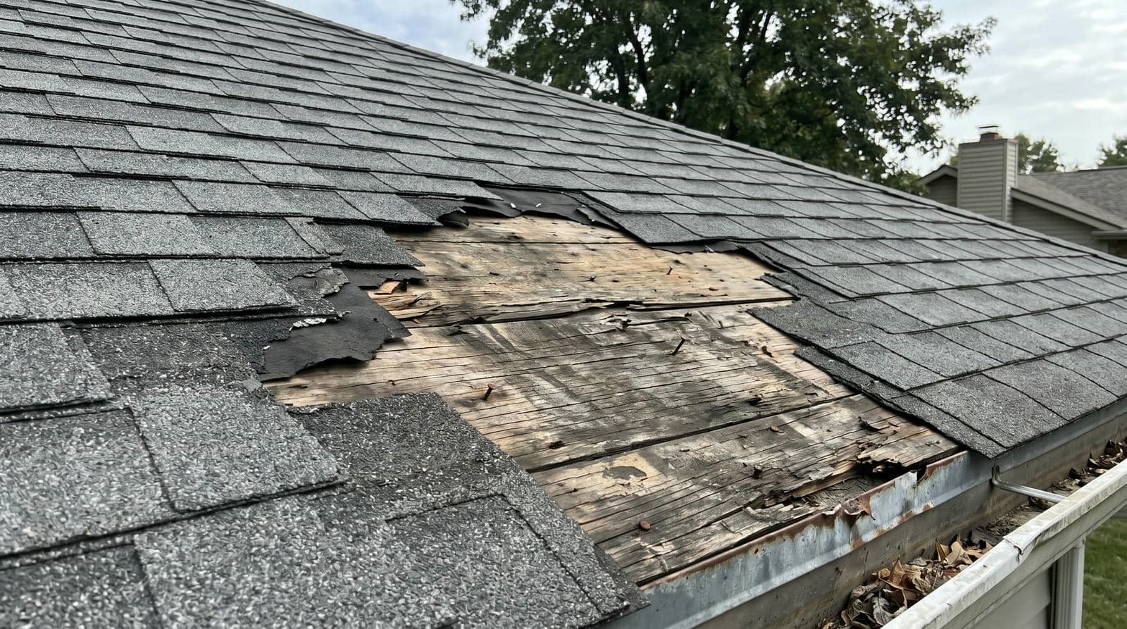 Roof with missing and damaged shingles exposing weathered wood underneath.