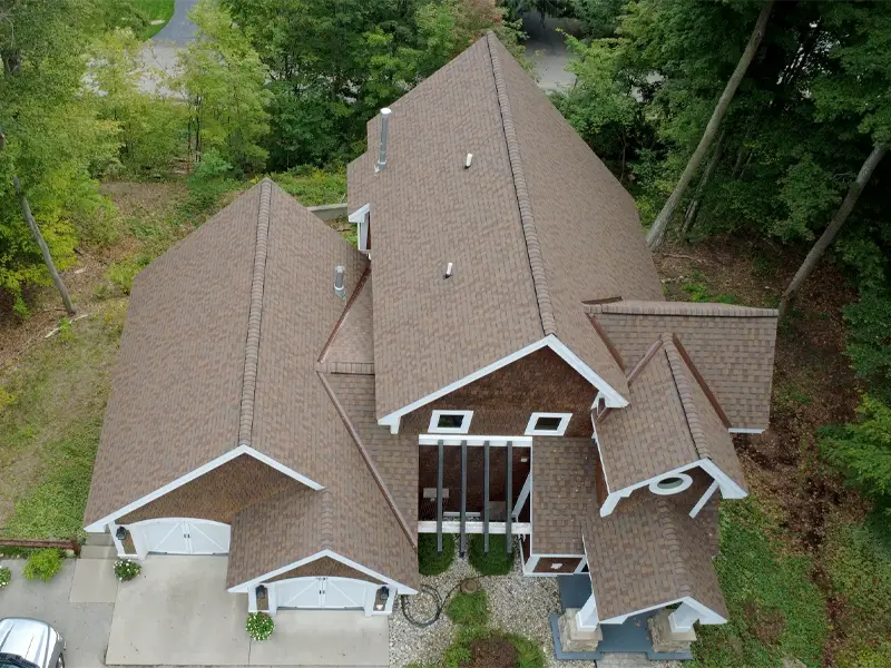 Aerial view of a large brown-roofed house surrounded by trees and greenery.