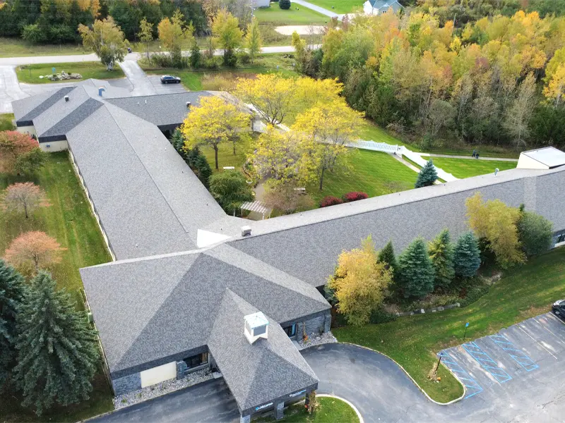 A large L-shaped building surrounded by trees with autumn foliage and adjacent parking spaces.