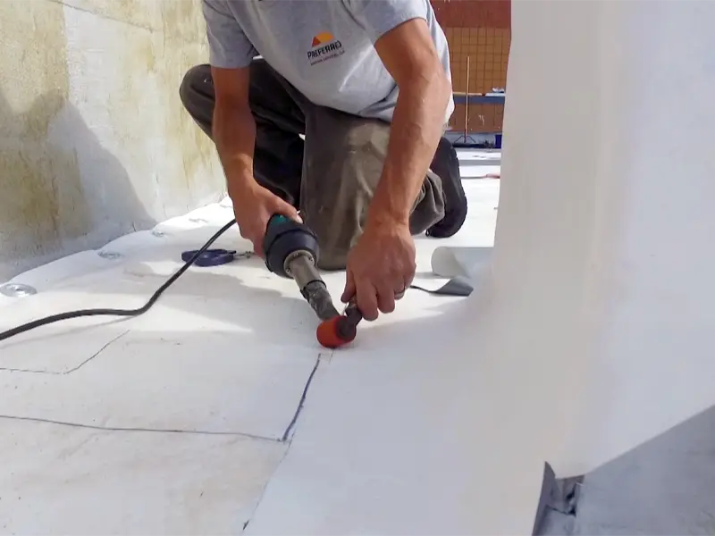 Person using a heat welding tool to seal seams on a white roofing membrane.