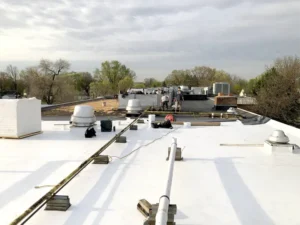 Workers installing a black roofing membrane on a flat roof with white roofing material in the foreground.