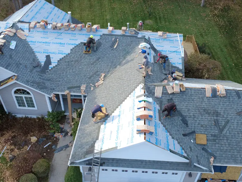 Workers installing shingles on a large house roof with underlayment visible.