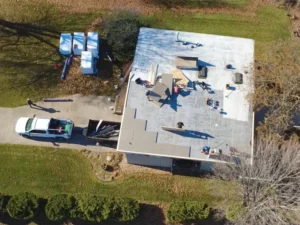 Workers installing a flat roof on a building with a truck and materials nearby.
