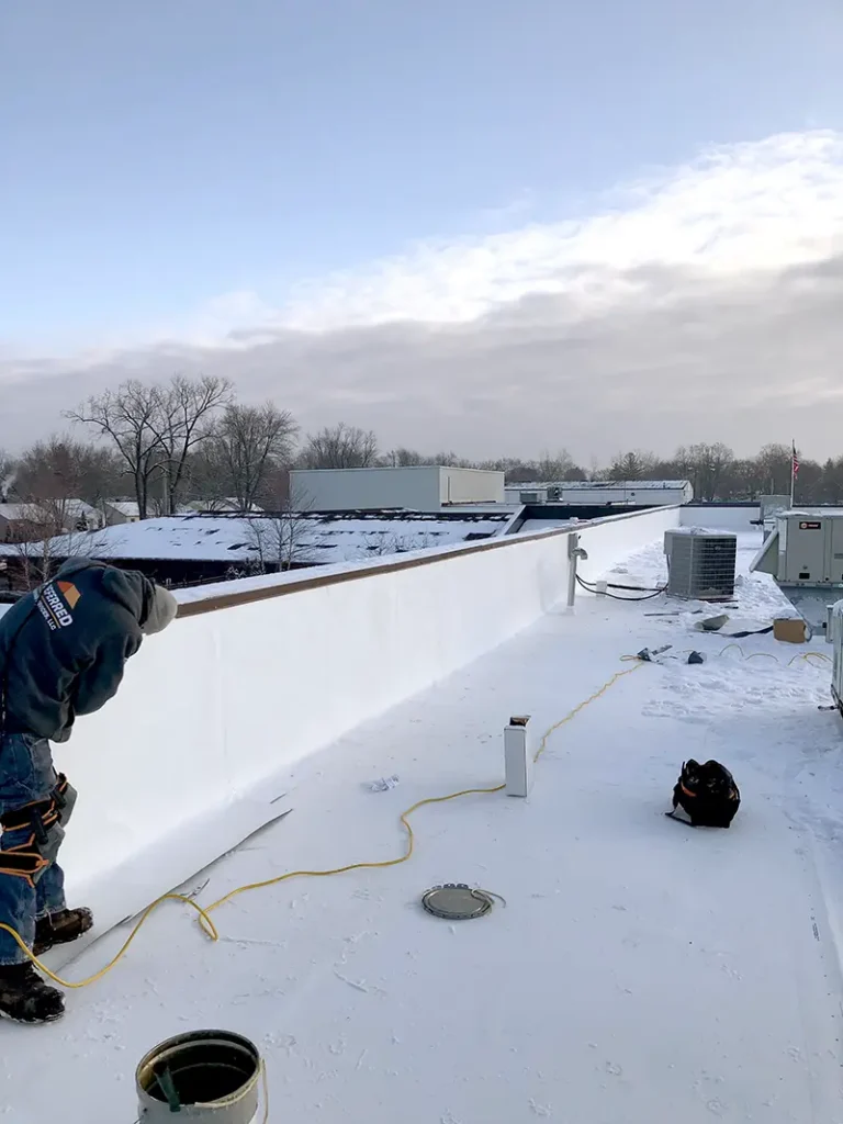 Worker installing or repairing a white roof membrane on a flat rooftop with tools and equipment nearby.
