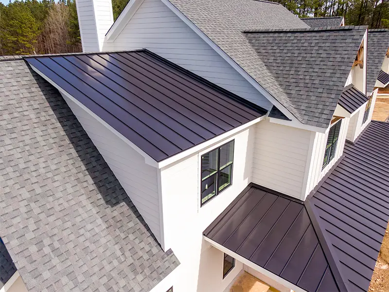 Modern house roof with dark metal and gray shingle sections viewed from above.
