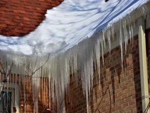 Long icicles hanging from a snow-covered roof edge above a brick wall.