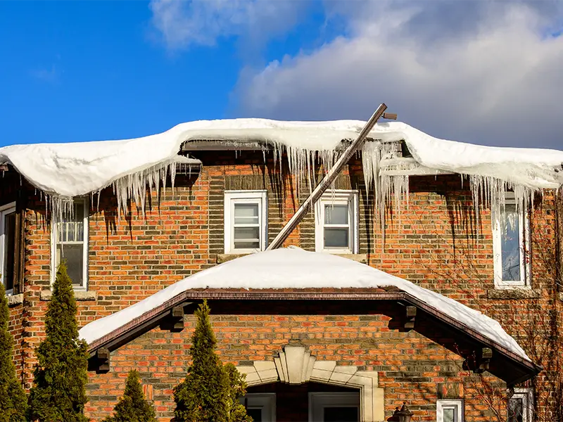 Brick house roof covered with snow and long icicles hanging from the eaves.