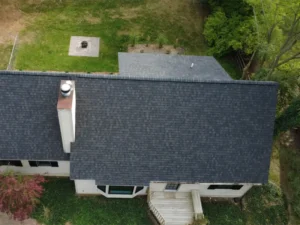 Aerial view of a house roof with a chimney and surrounding yard with grass and trees.