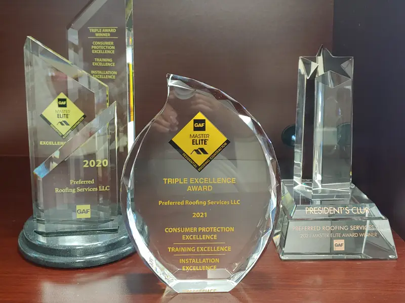 Three clear glass awards with yellow and black GAF Master Elite logos on a wooden surface.