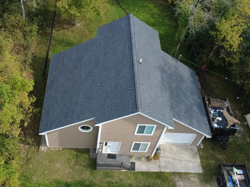 A two-story house with a gray roof and brown siding surrounded by trees and grass.