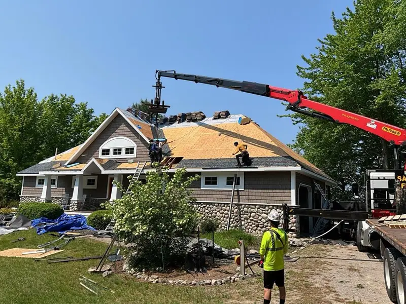 Workers installing a roof on a house using a crane and ladders on a sunny day.